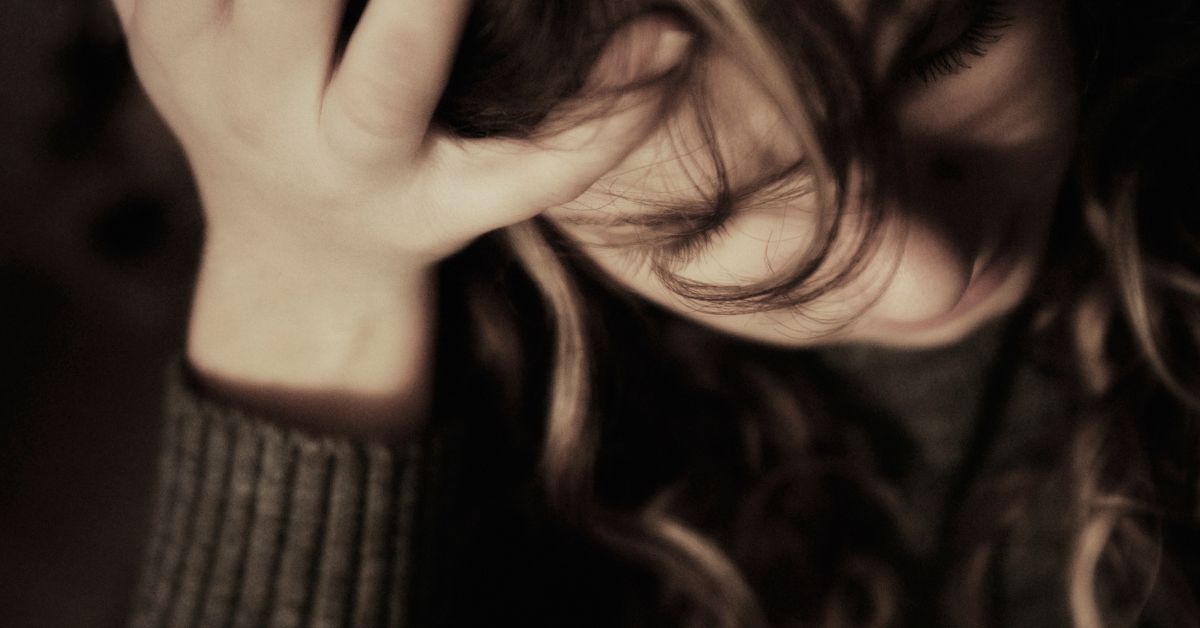 Close-up of a distressed woman with her head down and hand on her forehead, conveying sadness and emotional struggle.